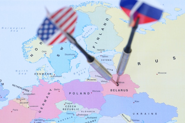 Deux fléchettes avec des drapeaux des Etats-Unis et de la Russie frappant la Biélorussie sur la carte du monde en gros plan