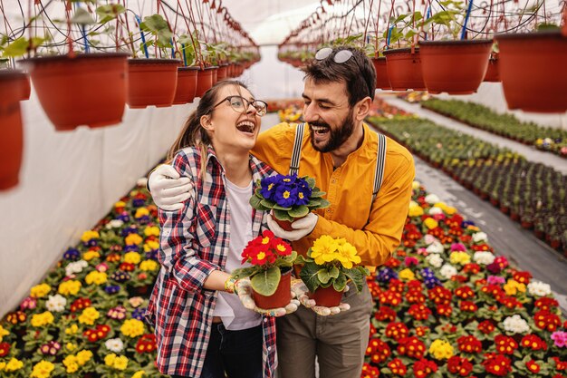 Deux fleurs de jardin de pépinière tenant des pots avec des fleurs, riant et étreignant. Tout autour se trouvent toutes sortes de fleurs colorées.