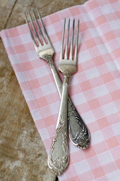 Deux fourchettes reposent sur une serviette rose. La composition se dresse sur un vieux fond en bois.