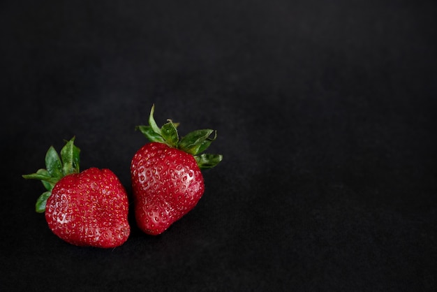 Deux fraises rouges mûres sur une surface noire