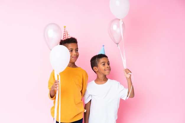 Deux frères afro-américains tenant des ballons sur un mur rose isolé