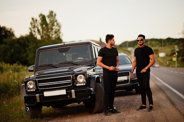 Deux frères asiatiques portent sur tout le noir posé près des voitures suv.