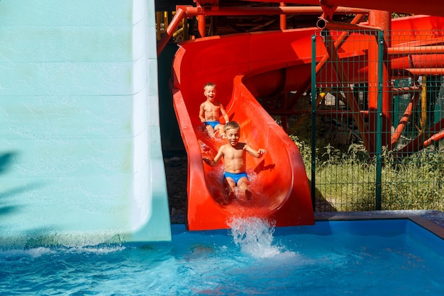 Deux frères jumeaux heureux glissent sur un toboggan aquatique