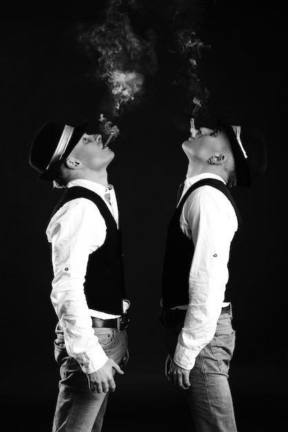 Deux frères jumeaux en style gangster posant. chapeaux, gilets, chemises blanches. blanc et noir.