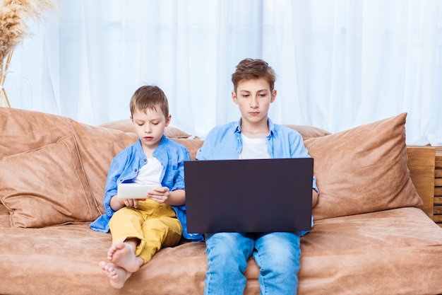 Deux frères naviguant sur Internet sur un ordinateur portable et une tablette. Style de vie moderne