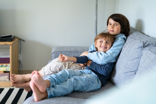 Deux frères sont assis sur un canapé à la maison. L'aîné embrasse le plus jeune. Frères et sœurs bonnes relations.