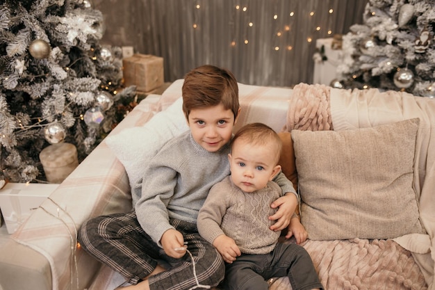 Deux frères sont assis sur le canapé et s'embrassent près du sapin de Noël