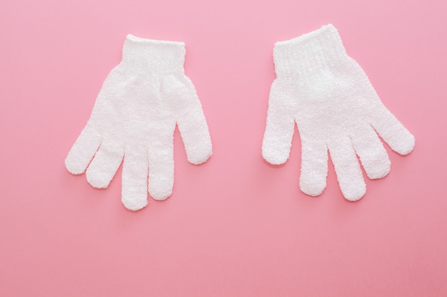 Photo deux gants de massage exfoliants pour la douche sur fond rose. gants à utiliser sous la douche pour le massage et le gommage.