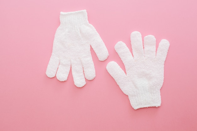 Deux gants de massage exfoliants pour la douche sur fond rose. Gants à utiliser sous la douche pour le massage et le gommage.