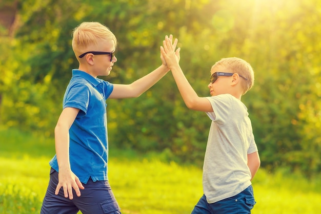 Deux garçons blonds en lunettes de soleil donnent cinq mains dans le parc ensoleillé