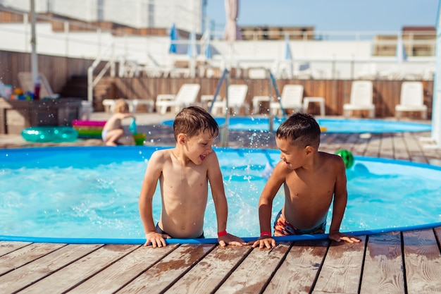 Deux garçons heureux et heureux de 6-7 ans qui se baignent dans la piscine en été en vacances près de l'hôtel. Caucasien et asiatique.