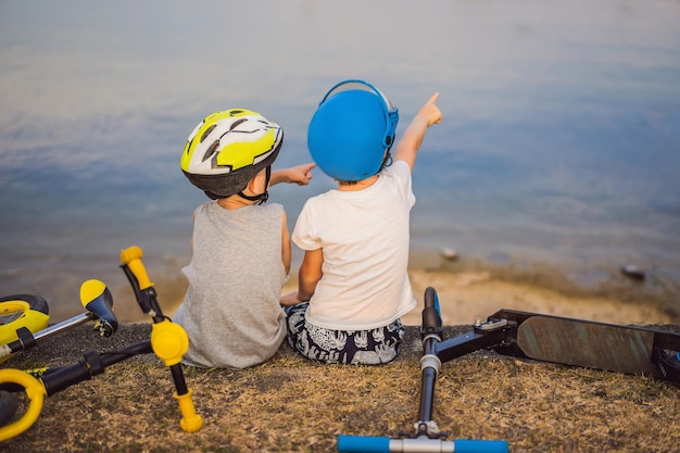 Deux garçons sont assis sur la rive du lac après avoir fait du vélo et du scooter