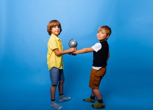 Deux garçons tiennent un globe sur fond bleu. concept d'éducation. espace de copie