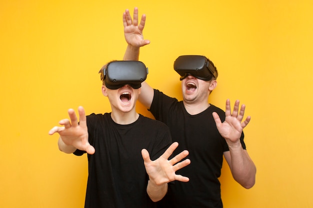 Deux gars dans des lunettes VR modernes jouent sur un fond jaune, une paire d'amis de joueurs dans des lunettes de réalité virtuelle