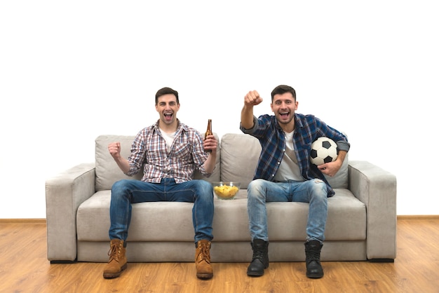 Les deux gars heureux avec une bière regardent un football sur le canapé