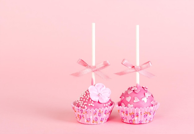 Deux gâteaux pop avec glaçage rose et décor sur fond rose