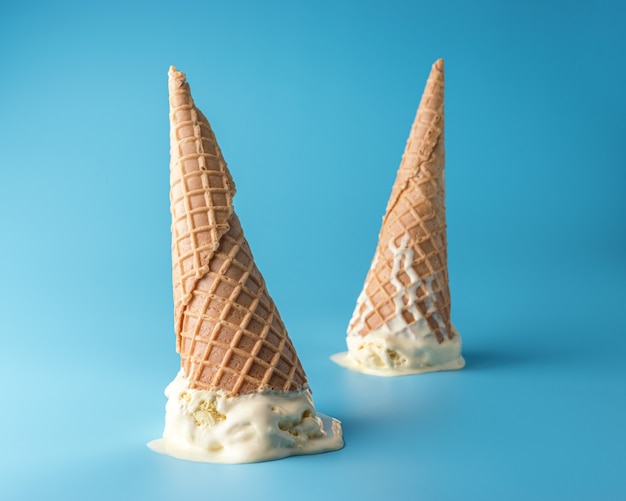 Deux glaces fondues avec des cornets de crème glacée sur fond bleu pastel