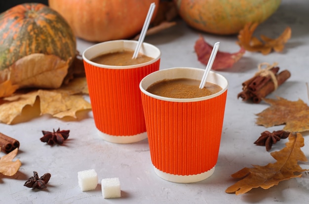 Deux gobelets en papier avec un délicieux latte à la citrouille et des épices sur une table grise avec des feuilles d'automne.