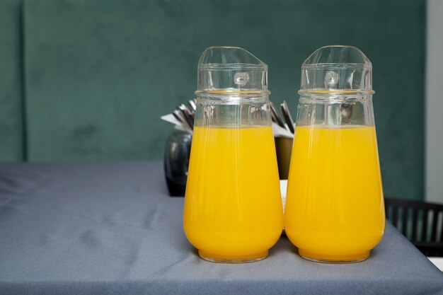 Deux grandes cruches transparentes de fruits boivent. Jus d'orange sur table grise.