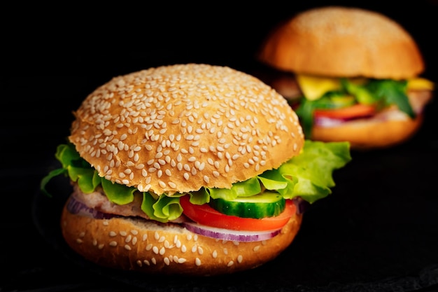 Deux gros hamburgers avec du boeuf et des légumes sur le fond sombre Des sandwichs frais et savoureux avec de la laitue verte Gros plan sur les aliments malsains