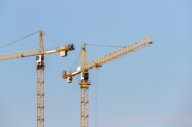 Deux grues à tour de construction jaune contre le ciel bleu