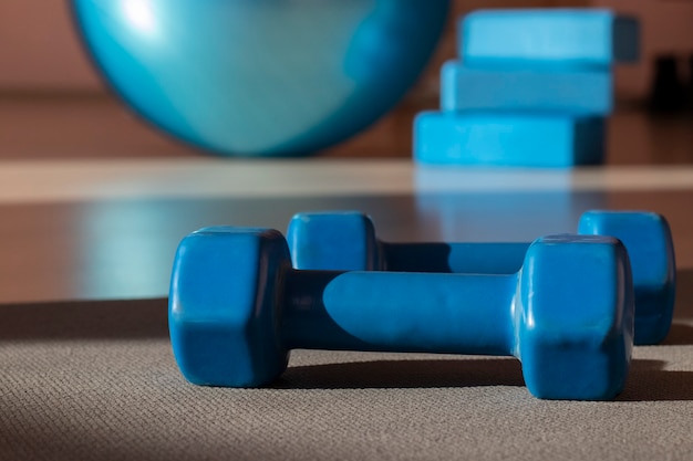 Deux haltères bleus sur un tapis de yoga gris, une balle et des cubes dans une salle de sport : concept de sport et de remise en forme. Fermer