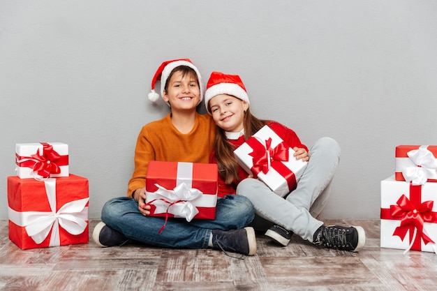 Deux heureux garçon et fille en chapeaux de père noël avec des coffrets cadeaux