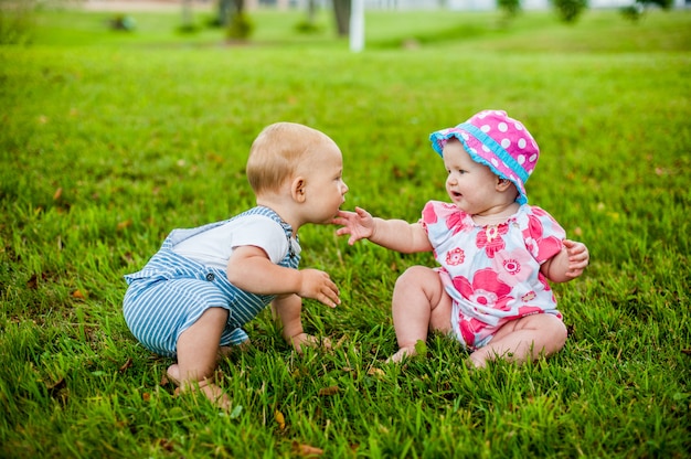 Deux heureux petit garçon et une fille de 9 mois, assis sur l'herbe et interagissent, parlent, se regardent.