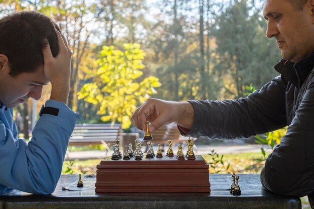 Deux hommes adultes jouent aux échecs à l'extérieur dans le parc. Vue de côté.