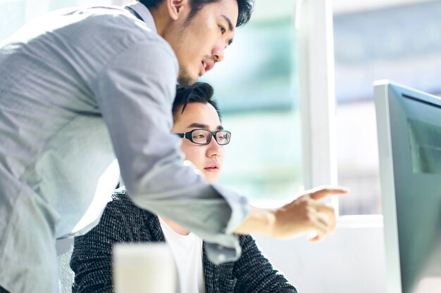 deux hommes d'affaires asiatiques travaillant ensemble dans un bureau en utilisant un PC de bureau