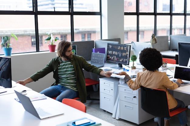 Deux hommes d'affaires divers travaillant dans un bureau de création. homme donnant un document à son collègue. des gens d'affaires et des collègues de travail dans un bureau de création très fréquenté.
