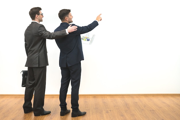 Les deux hommes d'affaires font un geste sur le fond du mur blanc