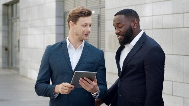 Deux hommes d'affaires heureux lisant de bonnes nouvelles sur une tablette numérique dans une ville moderne