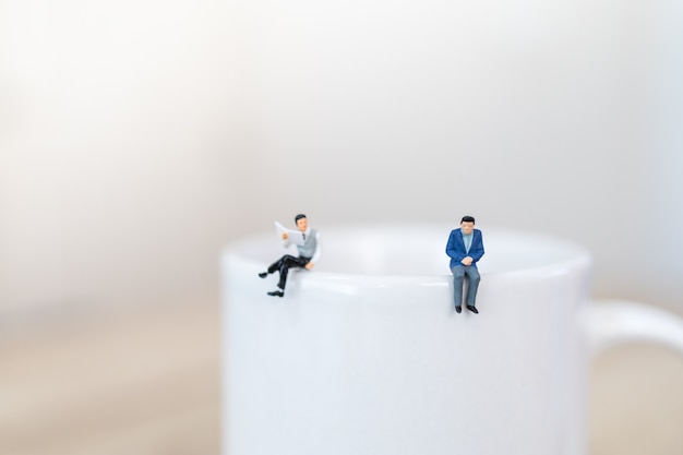 Deux hommes d'affaires miniatures figure debout sur le dessus de la tasse tasse blanche de café chaud avec distanciation sociale.