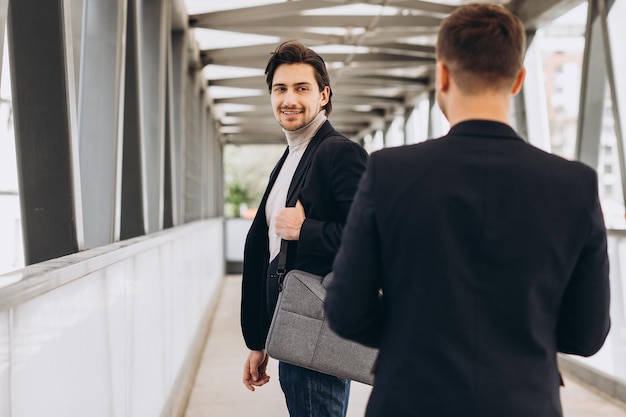 Deux hommes d'affaires modernes se saluent en souriant et en disant quelque chose sur fond de bureaux et de bâtiments urbains