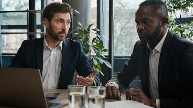 Deux hommes d'affaires multiraciaux dans le travail de bureau avec des données informatiques discutent d'un projet en ligne de démarrage