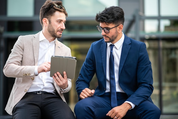 Photo deux hommes d'affaires ont une conversation sur un banc de rue occupés avec une tablette