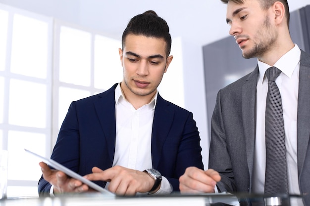 Deux hommes d'affaires ou partenaires travaillant avec une tablette au bureau dans un bureau moderne