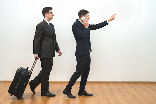 Les deux hommes d'affaires avec un téléphone de sac et un geste sur le fond de mur blanc