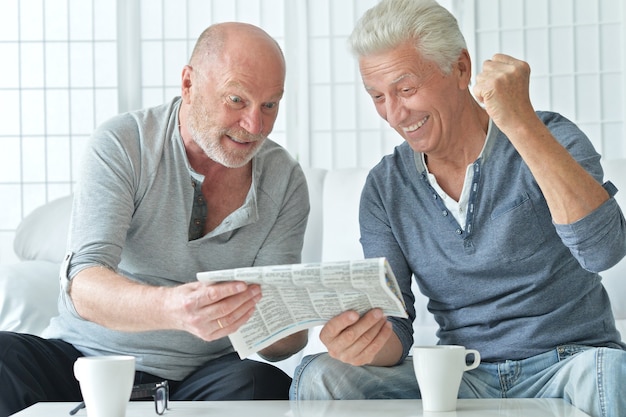 Deux hommes âgés avec du papier journal et du thé à la maison