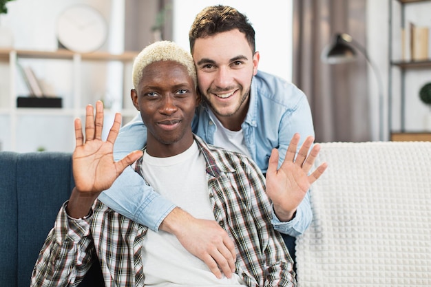 Deux hommes aimants agitant les mains et souriant devant la caméra à la maison