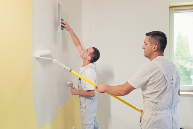 Deux hommes appliquent du plâtre sur le mur et réparent la maison