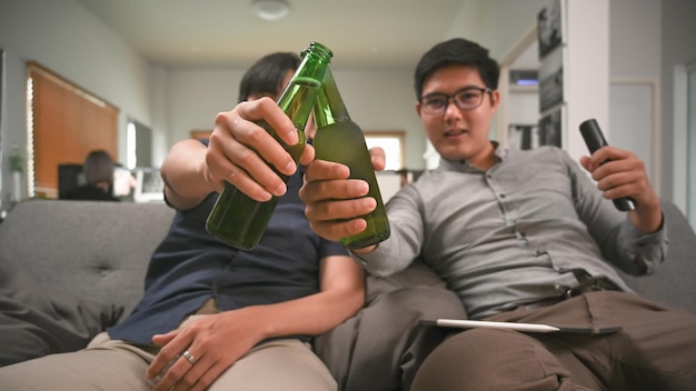 Deux hommes asiatiques buvant de la bière assis sur un canapé dans le salon