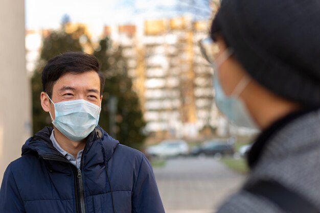 Photo deux hommes asiatiques dans des masques médicaux contre les sourires de covid-2019 et se parlent