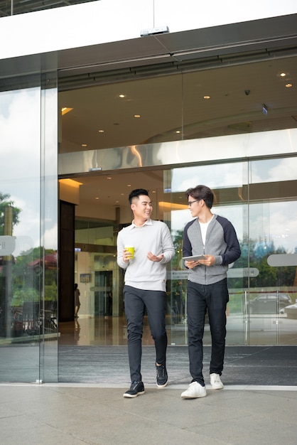 Deux hommes asiatiques parlent et utilisent un téléphone intelligent à l'extérieur du bâtiment]