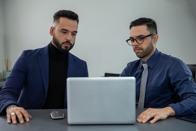 deux hommes assis dans un bureau devant l'ordinateur regardant l'ordinateur