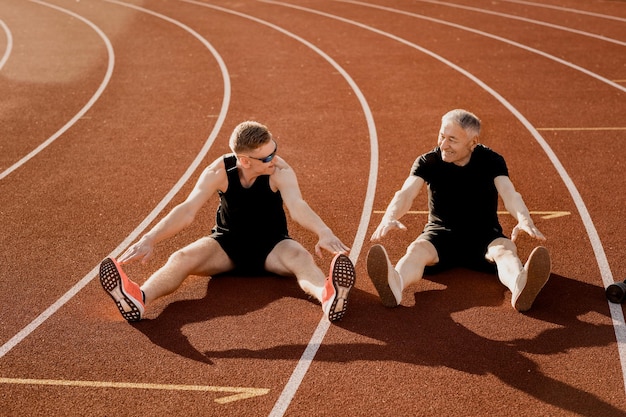 Deux hommes assis sur une piste, l'un d'eux s'étire.