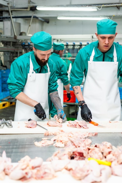 Deux hommes en blouse verte coupent de la viande dans une usine.