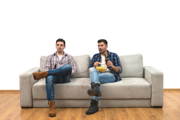 Les deux hommes boivent une bière sur le canapé sur un fond de mur blanc