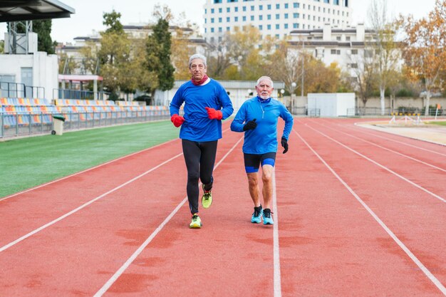 Deux hommes caucasiens âgés en vêtements de sport courant sur une piste d'athlétisme concentrés et en forme